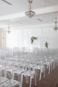 White Drapery and Piping | Asymmetrical Floral Arrangements with White Roses, Blue Flowers, and Greenery Wedding Ceremony Arch Ideas | Ghost Acrylic Chairs | Tampa Bay Kate Ryan Event Rentals | Florist Monarch Events and Design