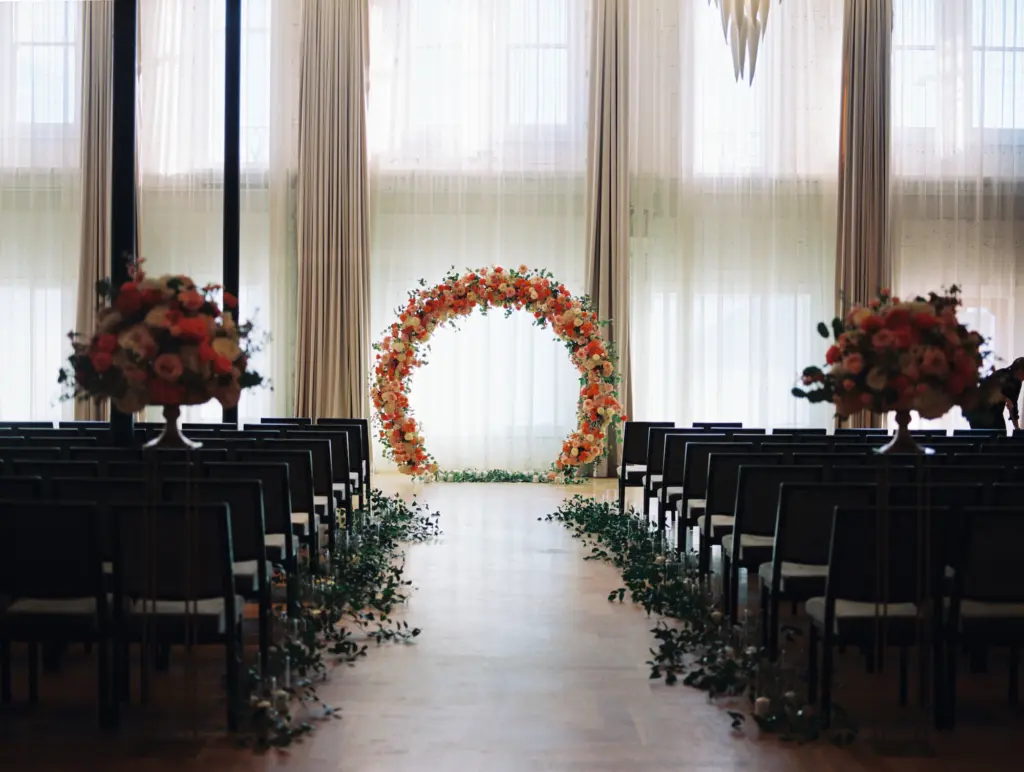 Valencia Ballroom with Large Windows | Round Orange, White, and Pink Floral Backdrop for Wedding Ceremony | Greenery Aisle Decor Ideas | Tampa Bay Venue Hotel Haya