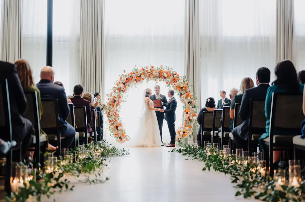 Bride and Groom Vow Exchange Wedding Portrait | Greenery and Candle Aisle Wedding Ceremony Decor Inspiration | Round Backdrop Ideas for Altar with Orange, Pink, and White Roses, Carnations, and Hydrangeas | Tampa Bay Photographer McNeile Photography | Planner Lemon Drops Weddings and Events | Venue Hotel Haya