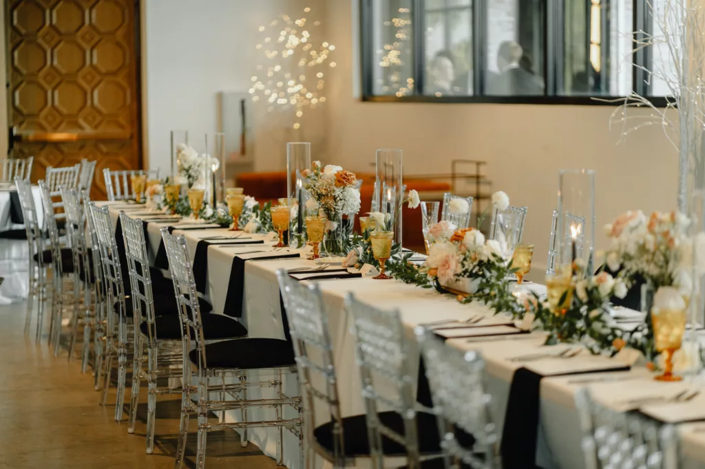 Timeless Black and White Wedding Reception Long Feasting Table Ideas | Ghost Acrylic Chair Seating Inspiration | Greenery Garland Centerpiece with Pink and White Roses | Tampa Bay Planner Coastal Coordinating | Kate Ryan Event Rentals