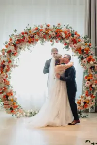 Bride and Groom First Kiss Wedding Portrait | Round Backdrop Ideas for Altar with Orange, Pink, and White Roses, Carnations, and Hydrangeas | Tampa Bay Photographer McNeile Photography | Planner Lemon Drops Weddings and Events