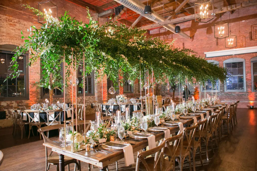 Tall Gold Stands with Greenery and White Flowers | Wooden Long Feasting Tables | Black and Gold Modern Wedding Ceremony Inspiration | Tampa Bay Kate Ryan Event Rentals