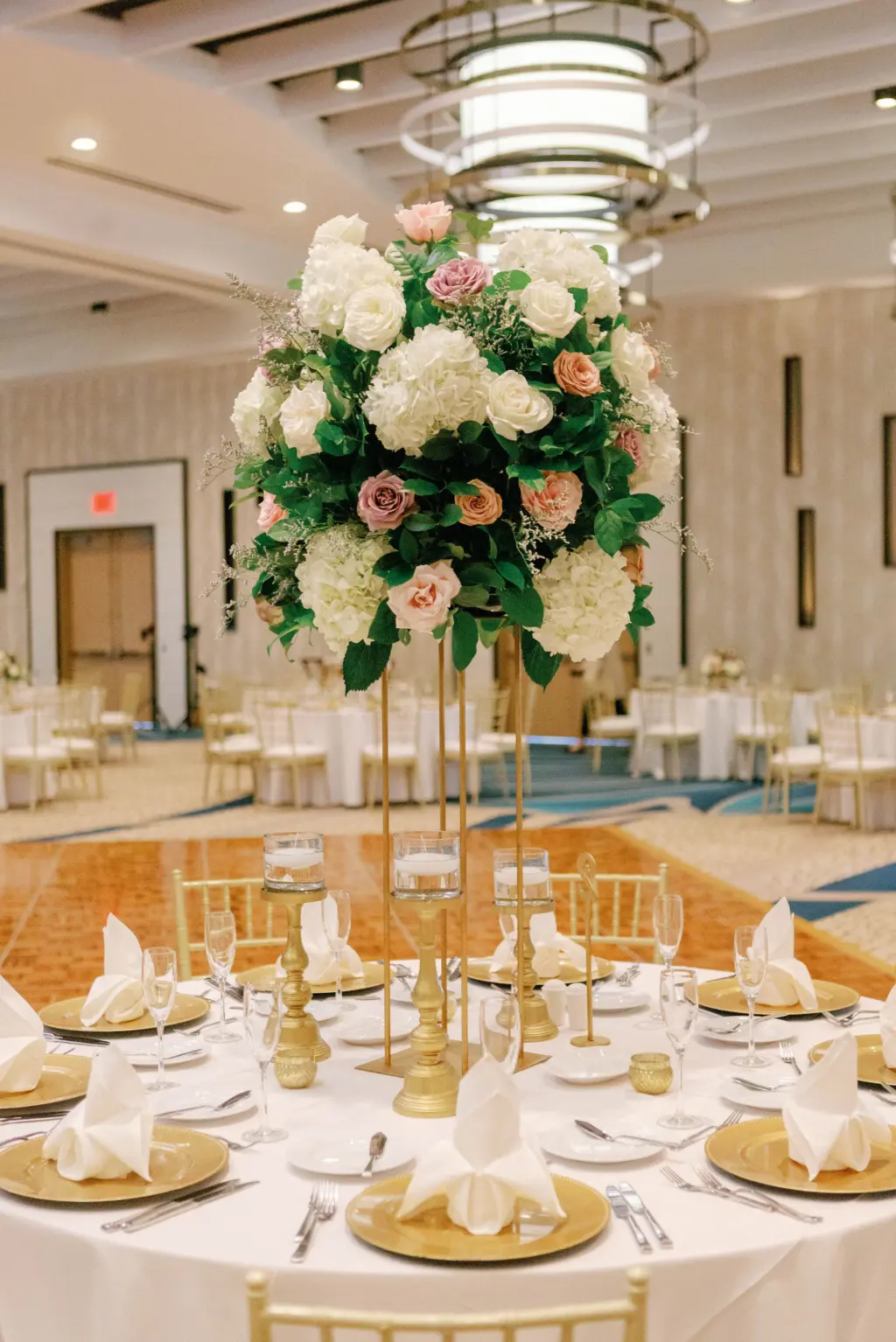 Elegant Gold Tablescape in Ballroom Wedding with Gold Chargers, White Linens, and Classic Florals in Tall Gold Centerpiece
