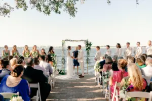 Bride and Groom Exchange Vows in Waterfront Wedding Ceremony in Front of Gold Arch with Greenery Tropical Ideas | Bradenton Waterfront Venue Pier 22 | Planner Breezin Weddings