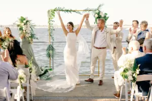Bride and Groom Just Married in Waterfront Wedding Ceremony in Front of Gold Arch with Greenery Tropical Details Wedding Portrait | Bradenton Waterfront Venue Pier 22 | Planner Breezin Weddings