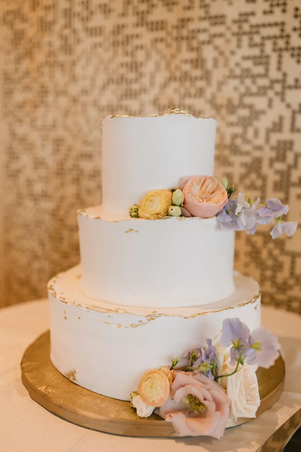 Three Tiered Round White Wedding Cake with Gold Deckle Edge and Pastel Pink, Blue, and Yellow Flower Accents