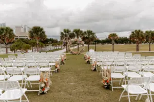Boho Outdoor Wedding Ceremony with White Folding Chairs | Orange and Pink Roses, Pampas Grass, and Greenery Aisle Flower Arrangement Inspiration | Venue Tampa River Center