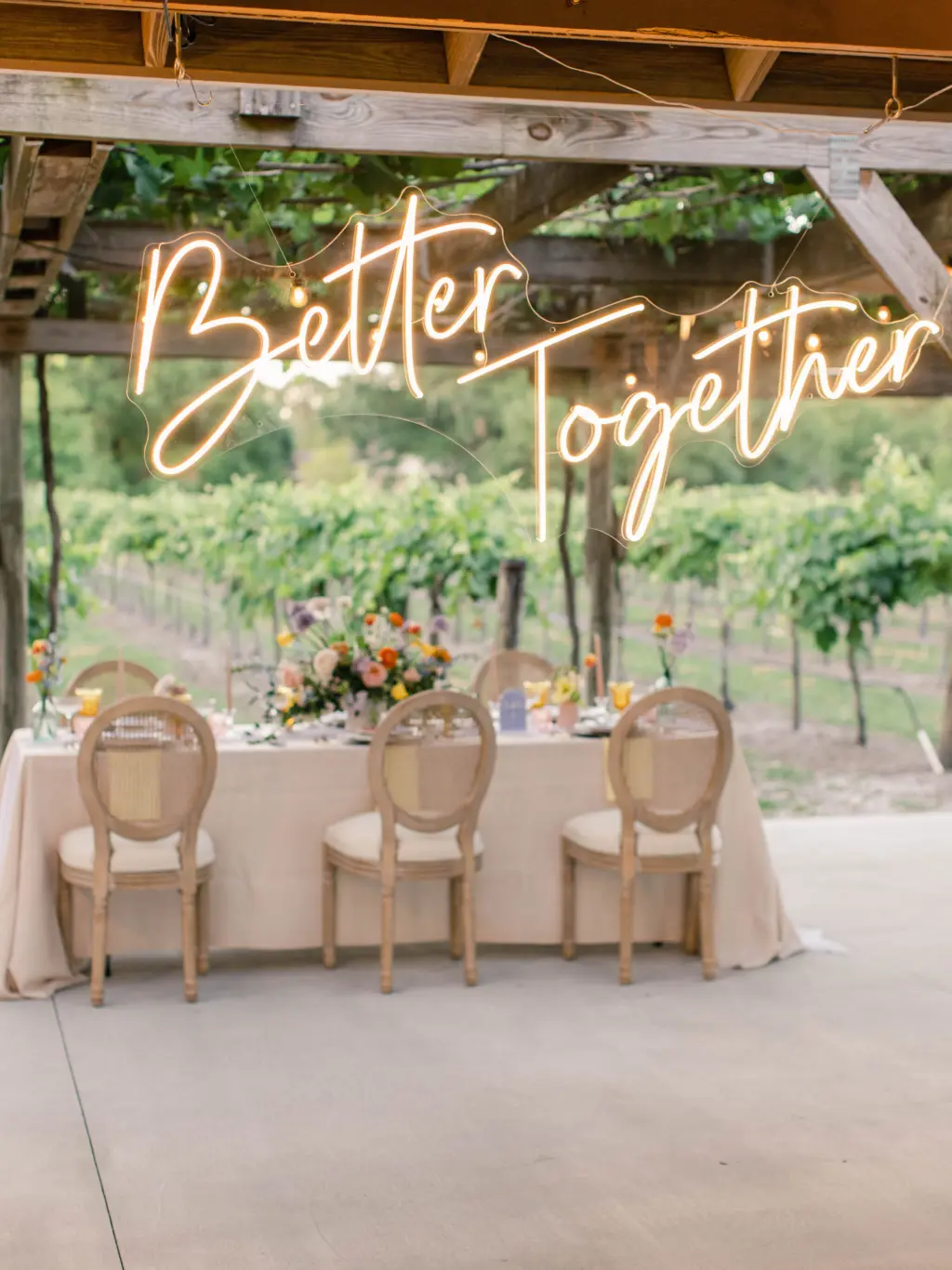 Better Together Neon Sign Backdrop Decor Inspiration for Spring Vineyard Wedding Reception | White Oak Cane Rattan Spring Wedding Reception Chair Inspiration with Long Feasting Table and Pastel Linen | Venue Fiorelli Winery | Colorful Whimsical Wedding Centerpiece Inspiration | Tampa Bay St. Petersburg Florist Save The Date Florida