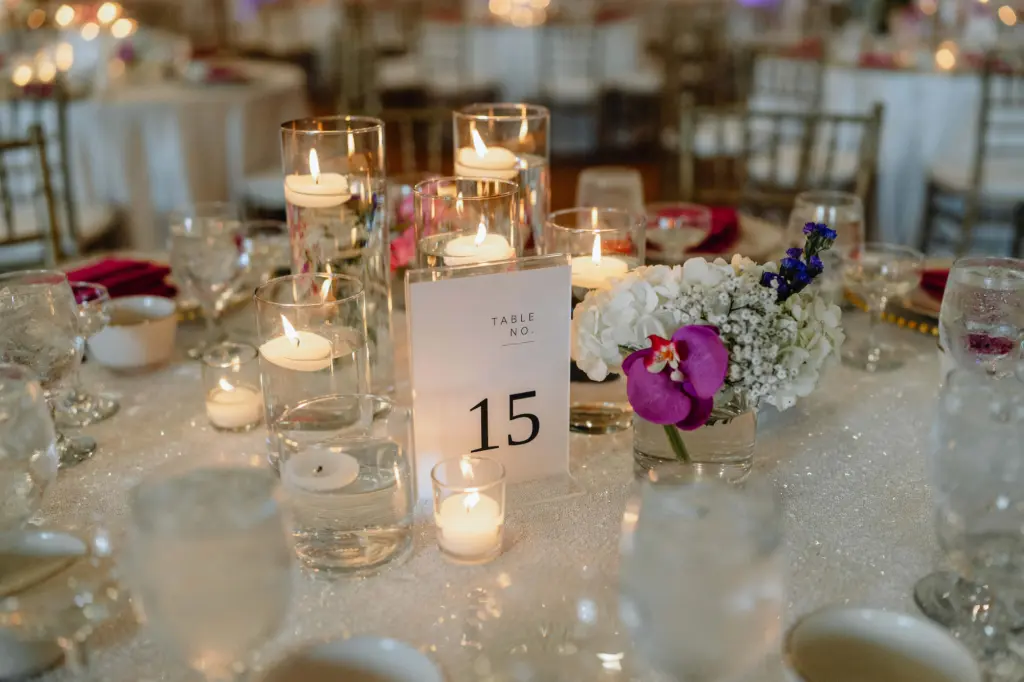 White Acrylic Table Numbers with Black Lettering in Tropical Wedding | Reception Centerpieces with Purple Orchids and White Floral Detailing and Floating Candles in Asian Fusion Wedding Décor