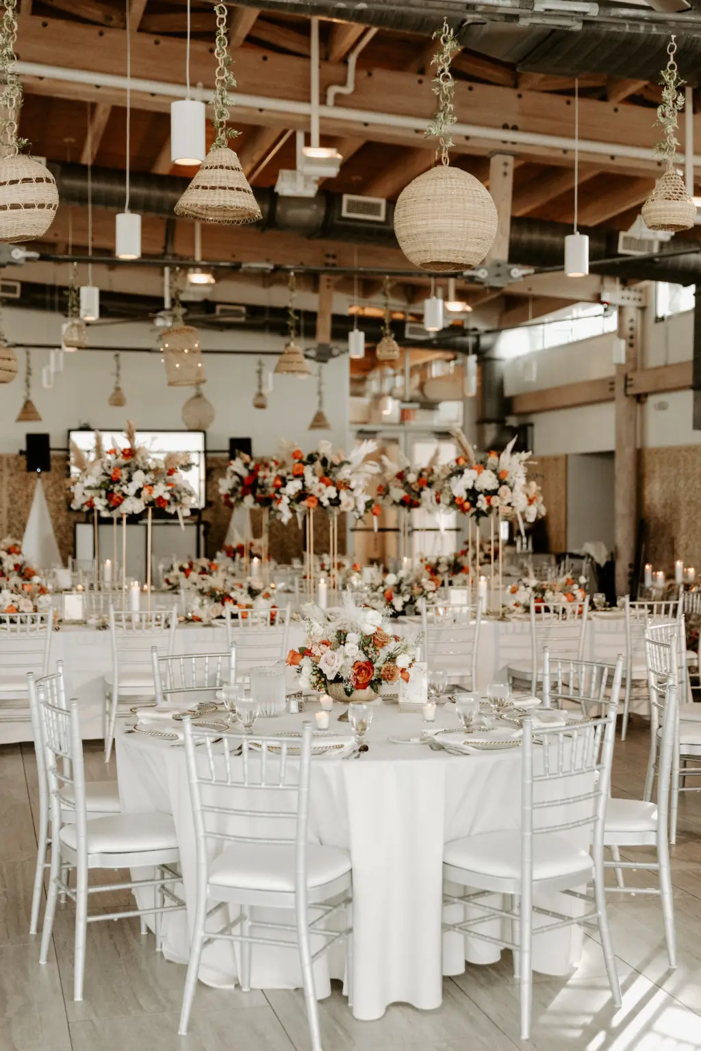 Boho Wedding Reception Inspiration | Rattan Hanging Lanterns | Silver Chiavari Chairs with White Linen and Long Feasting Tables | Orange, Pink, and White Roses with Greenery Centerpiece Ideas | Downtown Tampa Planner Breezin Weddings