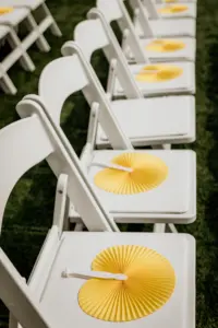 White Folding Ceremony Chairs with Yellow Fans for Guest During Outdoor Wedding Beach Ceremony