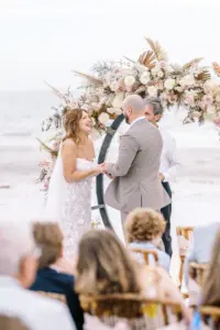 Bride and Groom Exchange Vows in Front of Floral Arch in Beach Wedding Ceremony Inspiration