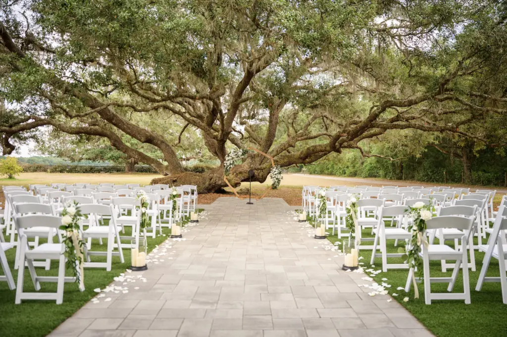 Wedding Ceremony Tree Inspiration | Geometric Wooden Arch | White Folding Garden Chairs | Candle and White Rose Petal Aisle Decor Ideas | Tampa Bay Event Venue Legacy Lane Weddings