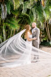 Bride and Groom Tropical Wedding Portrait with Long Train Veil | Dany Tabet Strapless Lace Floral Fit and Flare Tulle Bridal Gown | Beige Grey Taupe Groom Suit