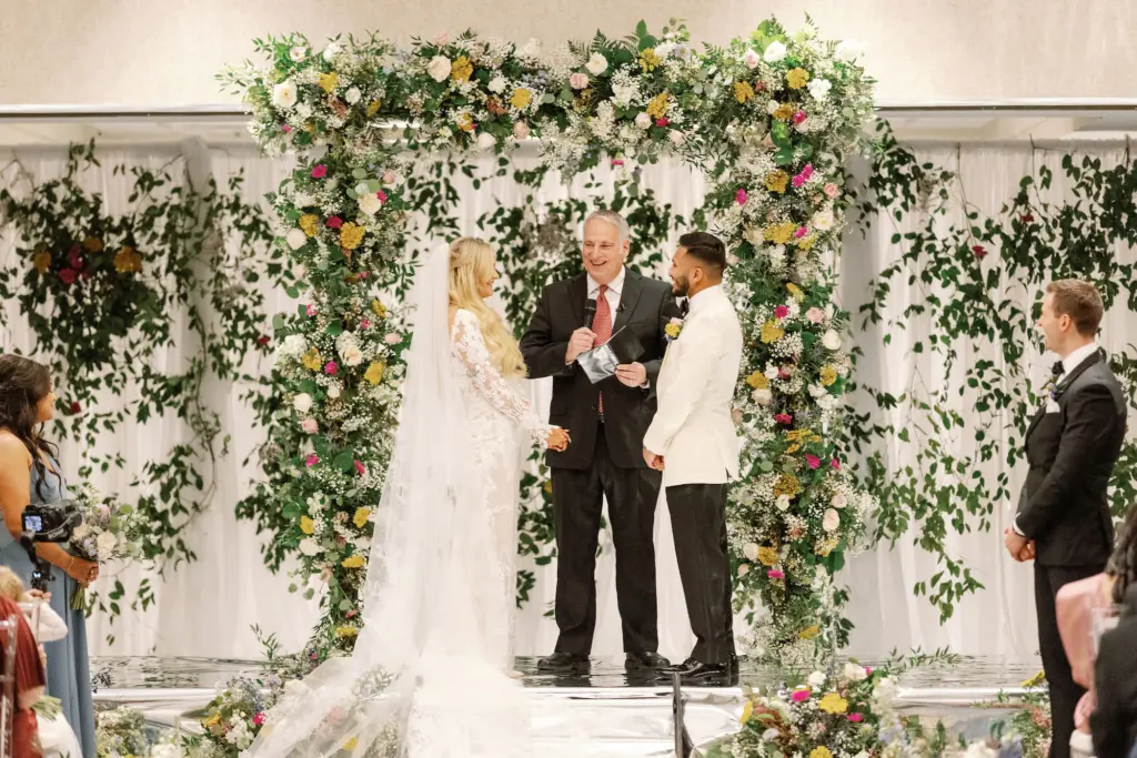 Bride and Groom Exchanging Vows | Pink, Yellow, and White Spring Flowers Arch Inspiration | Colorful Indian Fusion Wedding Ceremony | Tampa Bay Florist Lemon Drops Weddings & Events