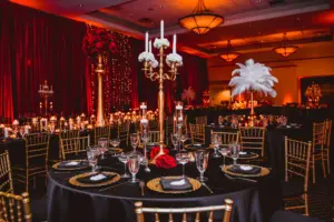 Black Linen Table Cloth with Gold Chiavari Chairs and Chargers | Tall Gold Centerpieces with Candles and White Florals and Feathers 1920s Tablescape Inspiration | Tampa Rental Company A Chair Affair | Downtown St. Petersburg Florida Event Venue Mahaffey Theatre