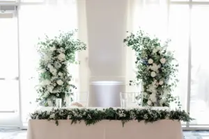 White Roses, Baby's Breath, Hydrangeas, Blue Delphinium, Eucalyptus, and Greenery Floral Backdrop for Sweetheart Table | White and Blue Wedding Reception Decor Ideas | Clear Acrylic Chiavari Chairs | Tampa Bay Event Planner Coastal Coordinating