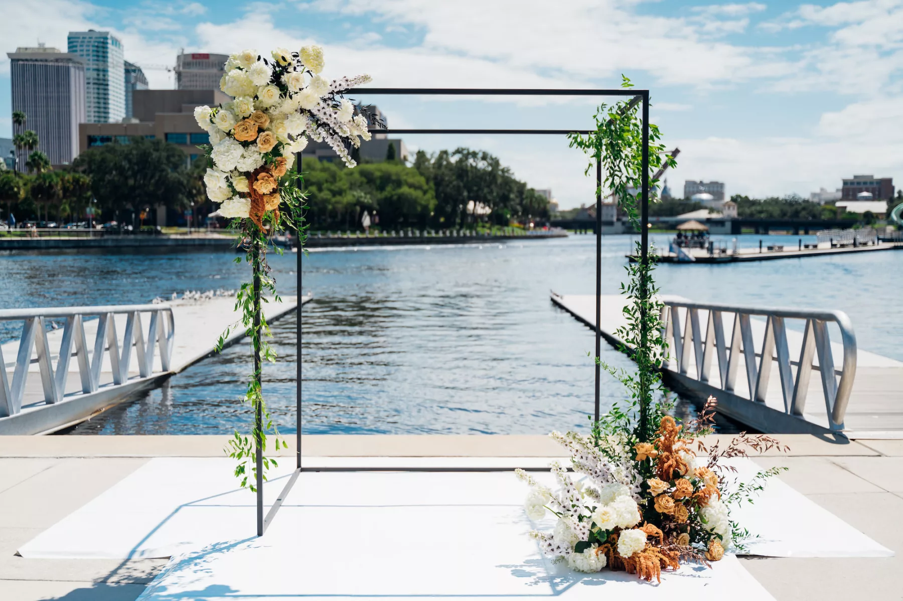 Modern Black Ceremony Arch with White Hydrangeas, Orange Roses, Orange Veronica, and Greenery | Fall Waterfront Wedding Ceremony Flower Arrangement Decor Ideas | Venue Tampa River Center