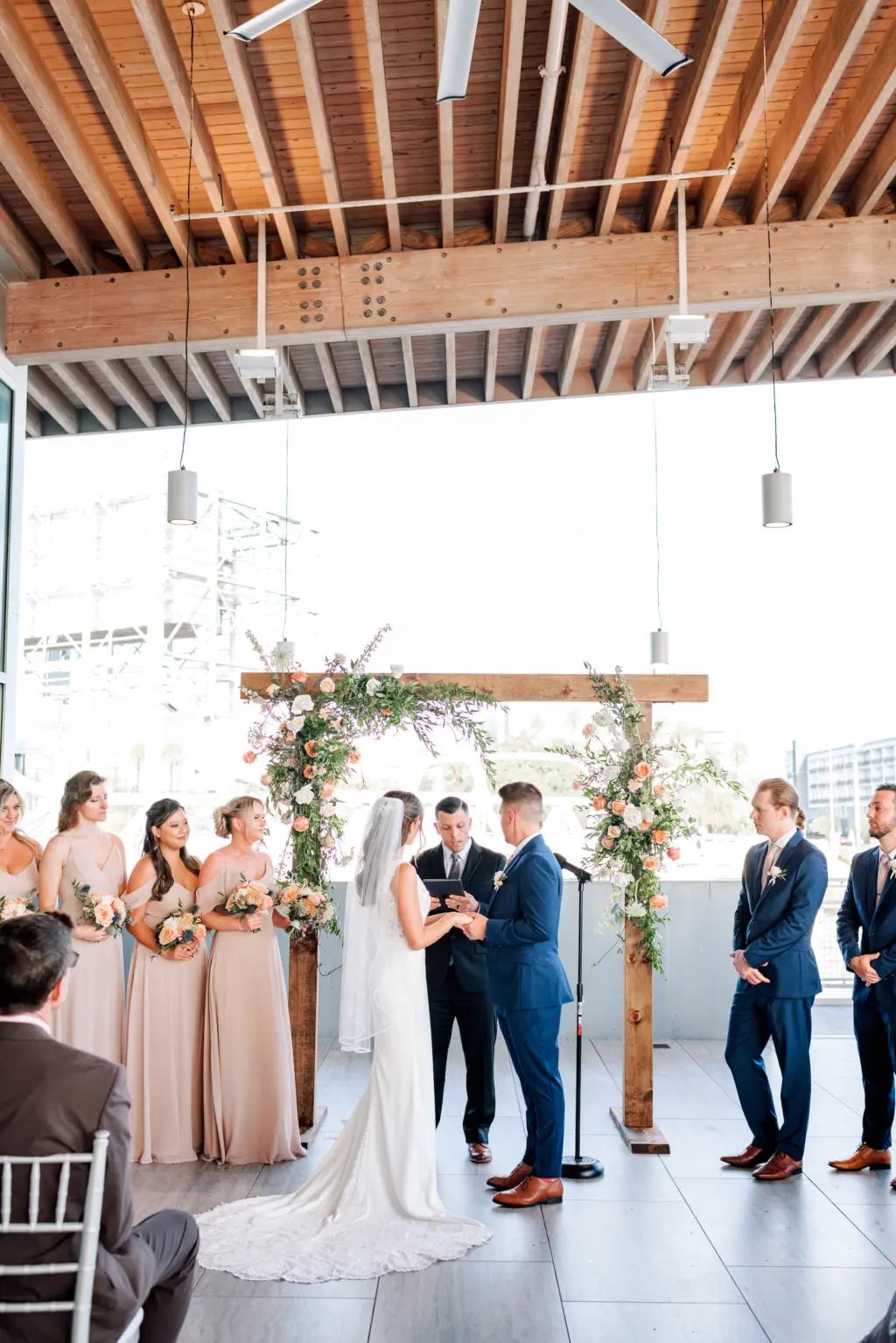 Bride and Groom Vow Exchange Wedding Portrait | Rustic Wooden Arch with Pink, Orange, and White Roses and Greenery Ceremony Decor Ideas | Venue Tampa River Center