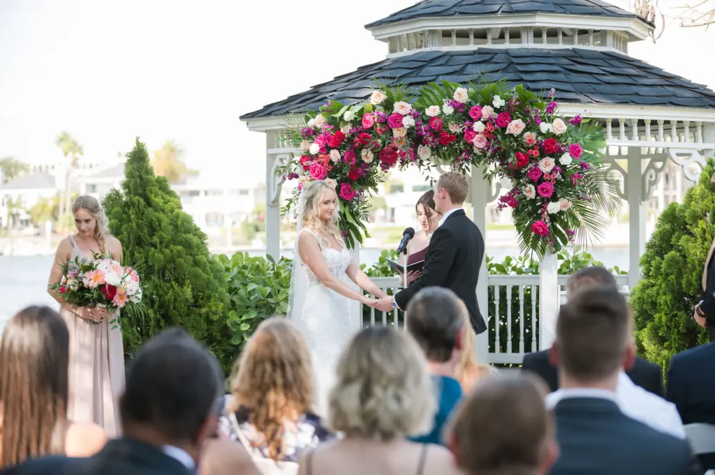 Bride and Groom Wedding Vow Exchange | Red, Pink, Orange, and White Roses with Greenery Altar Arch Inspiration | Tampa Waterfront Venue Davis Islands Garden Club