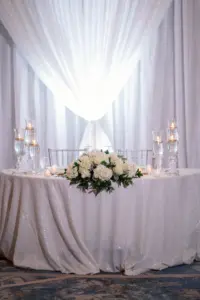 White Pipe and Drape Drapery for Elegant Wedding Reception Sweetheart Table Decor Ideas | Floating Candles, Roses and Hydrangea Tabletop Flower Arrangement Inspiration