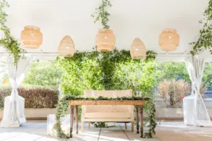 Sweetheart Table with Tufted Loveseat, Wooden Farm Table, Greenery Garland, Boho Chandeliers, and Floor Candle Decor Inspiration | Tented Wedding Reception Ideas | Tampa Bay Kate Ryan Event Rentals