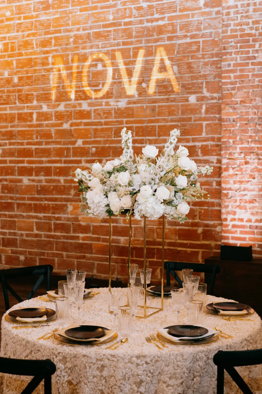 Tall Gold Flower Stand Centerpiece Inspiration with White Roses, Stock Flowers, and Hydrangeas | Black and Gold Table Setting Ideas for Modern Great Gatsby Themed Wedding Reception Ideas | Black Chairs | St Pete Kate Ryan Event Rentals | Florist Marigold Flower Co