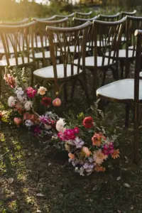 Boho Golden Hour Wedding Ceremony Inspiration | Whimsical Flower Aisle Decor Ideas | Wooden Chairs | Pink Roses, Orange Chrysanthemums, Wild Flowers, and Greenery