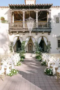 Glamorous White and Gold Outdoor Wedding Ceremony with Drapery Decor and Crystal Chandelier String Light Inspiration | Gold Chiavari Chairs with Organza Sashes and White Roses and Greenery Aisle Flower Arrangements | Sarasota Event Venue Powel Crosley Estate