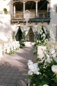 Glamorous White and Gold Outdoor Wedding Ceremony with Drapery Decor and Crystal Chandelier String Light Inspiration | Gold Chiavari Chairs with Organza Sashes and White Roses and Greenery Aisle Flower Arrangements | Sarasota Event Venue Powel Crosley Estate
