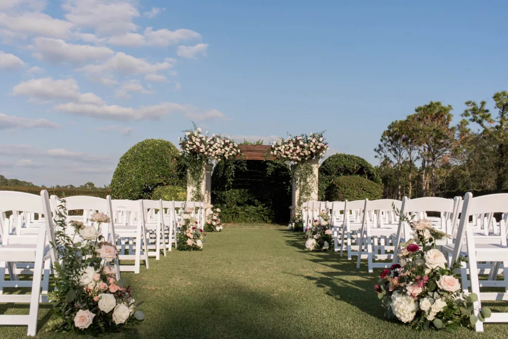 Luxurious Outdoor Wedding Ceremony on the Event Lawn Inspiration | White and Pink Roses, Hydrangeas, Chrysanthemums, and Greenery Aisle Decor Ideas | White Folding Garden Chairs | Tampa Bay Venue The Concession Golf Club | Planner Parties A La Carte | Florist Bruce Wayne Florals