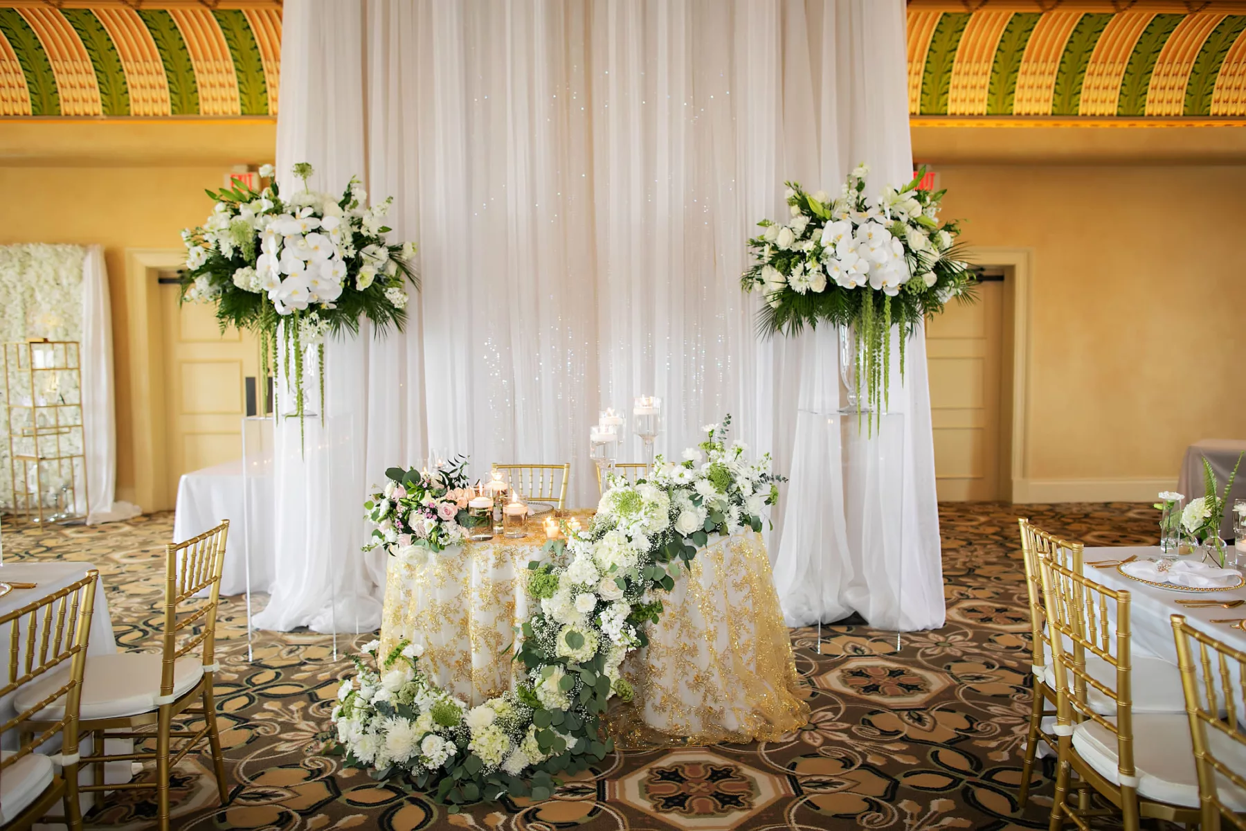 Classic White Wedding Reception Decor Ideas | White Drapery Sweetheart Table Backdrop Inspiration | Gold Sequin Tablecloth | White Orchid, Baby's Breath, Roses, and Greenery Floral Arrangement Ideas | Tampa Bay Event Planner Coastal Coordinating