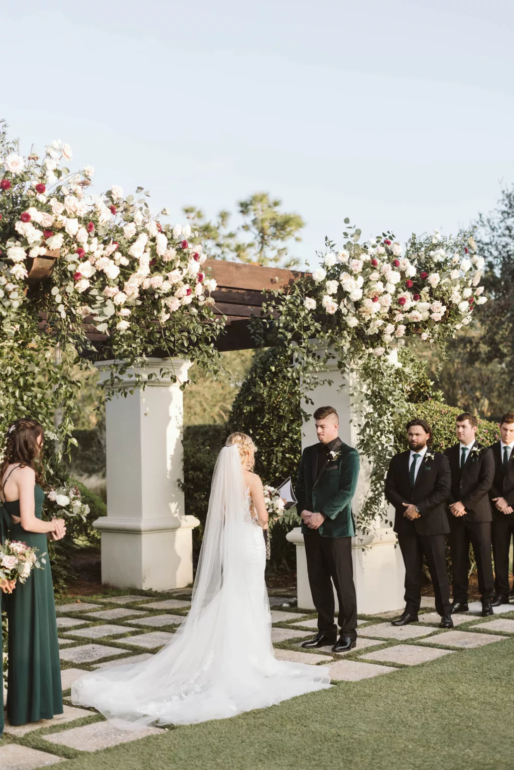 Luxurious Emerald Green Outdoor Wedding Ceremony on the Event Lawn | Pergola with White Roses, Purple Chrysanthemums, and Cascading Greenery Decor Inspiration | Tampa Bay Venue The Concession Golf Club | Florist Bruce Wayne Florals