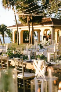 Glamorous Outdoor Wedding Reception Decor Ideas | Greenery Garland and White Candle Centerpiece Inspiration | Gold Chiavari Chairs and Wood Farm Feasting Tables under Canopy String Lights