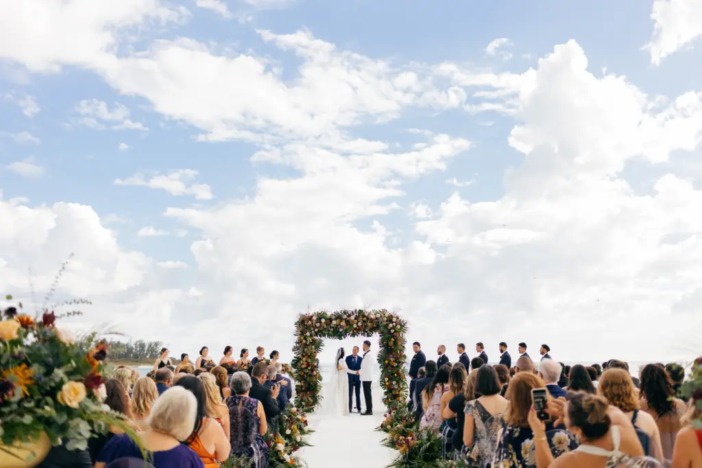 Bride and Groom Vow Exchange | Tropical Fall Moody Black Tie Beach Wedding Ceremony Arch Inspiration | White, Yellow, and Blush Roses, Burgundy Chrysanthemums, Monstera Leaves, and Palm Leaves | Sarasota Event Venue The Resort at Longboat Key Club
