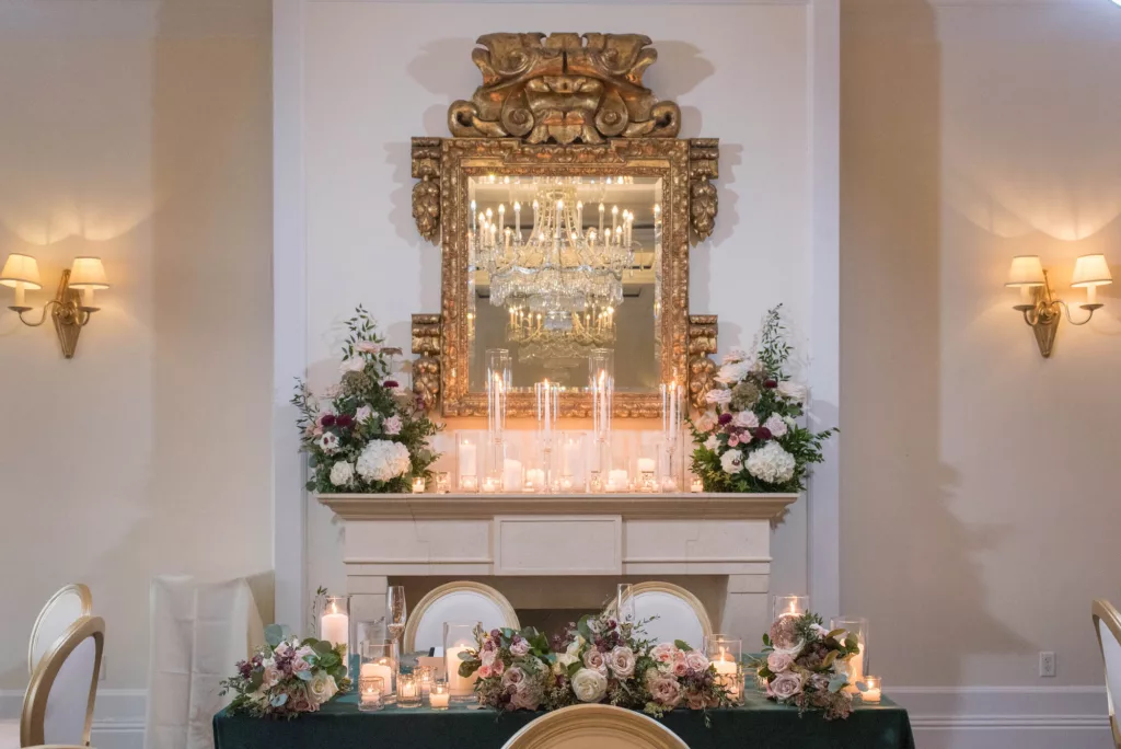 Luxurious Emerald, Mauve, and White Wedding Reception Sweetheart Table Decor Inspiration | Gold Mirror Mantle with Taper and Pillar Candles | White and Pink Roses, Hydrangeas, Chrysanthemums, and Greenery Flower Arrangement Ideas | Tampa Bay Florist Bruce Wayne Florals