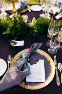 Dark Moody Fall Wedding Reception Table Setting Inspiration | Deep Dark Purple Eggplant Table Linen with Gold Glass Charger Plate and Iridescent Napkin