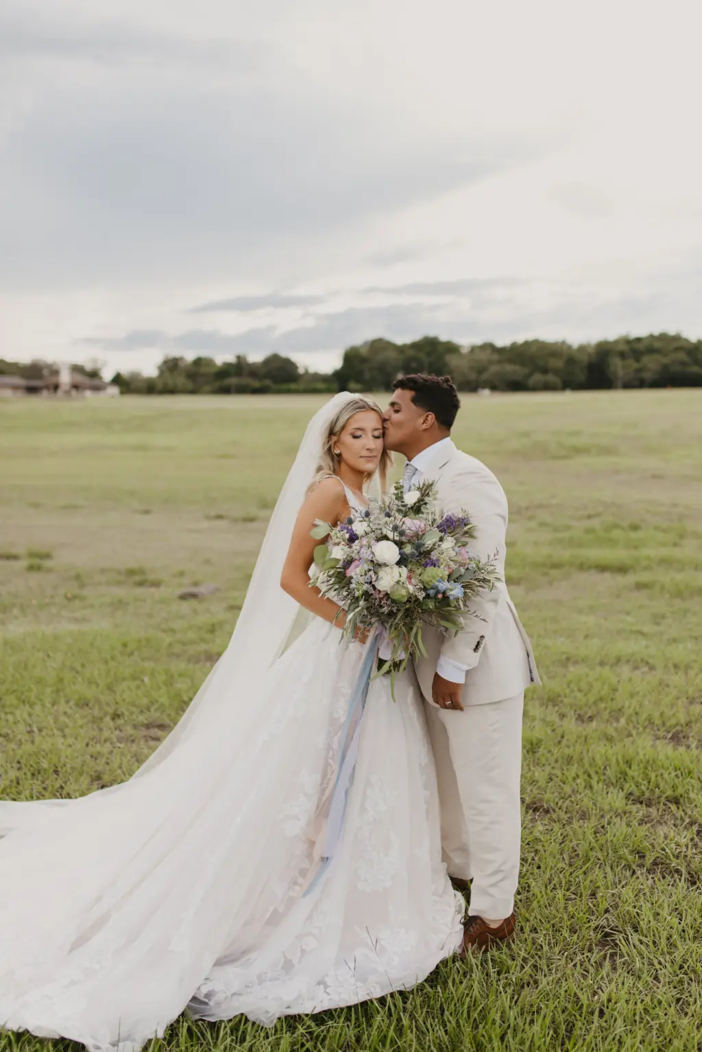 Romantic Bride and Groom in a Field Wedding Portrait | White Open Back Lace and Tulle Lillian West Wedding Dress with Maggie Sottero Veil Inspiration | Cream Groom's Suit | Pastel Bridal Bouquet with White Roses, Eucalyptus, Blue Thistle, and Greenery Ideas | Tampa Bay Photographer Valentina Rose Photography | Event Venue Simpson Lakes | Planner EventFull Weddings
