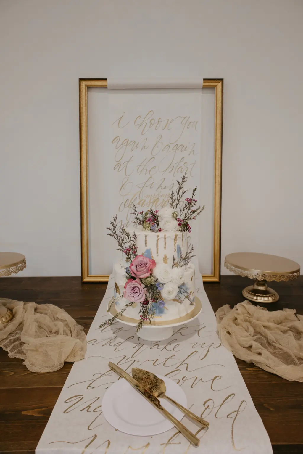 I Choose You Again and Again Calligraphy Hand-lettered Script Font Scroll Inspiration for Cake Table | Two-Tiered White Buttercream Abstract Wedding Cake with Gold Foil and Light Blue Icing, Pink and White Rose Accents