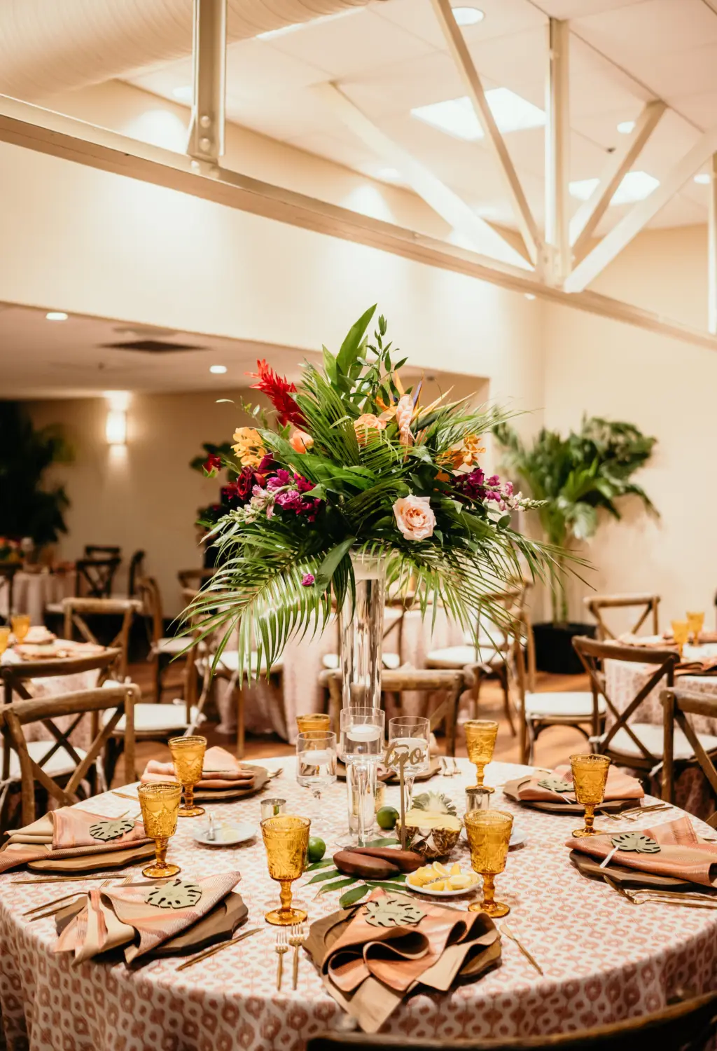 Tropical Wedding Reception Centerpiece Decor Inspiration | Tall Floral Arrangement with Palm Leaf, Pink and Burgundy Roses, Birds of Paradise | St Pete Florist Save The Date Florida | Wood Charger Plates and Vintage Glassware from Kate Ryan Event Rentals