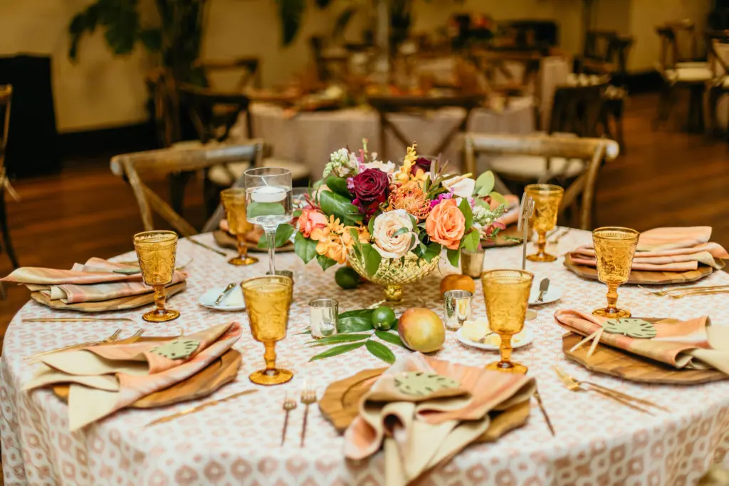 Tropical Boho Wedding Reception Inspiration | Amber Colored Glassware Goblets and Retro Neutral Linen by Kate Ryan Event Rentals | Peach, Blush, and Burgundy Roses, with Protea, Greenery, Mango, and Lime Centerpiece Decor Ideas | St. Pete Florist Save The Date Florida