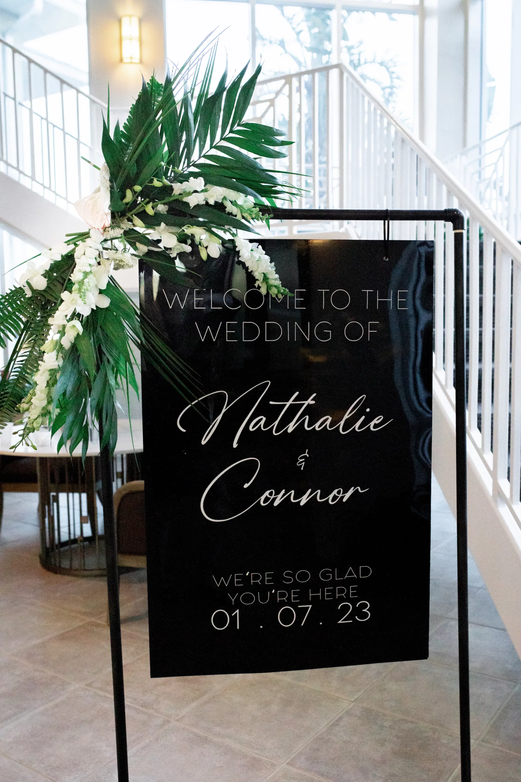Modern Black and White Welcome Wedding Ceremony Sign Ideas | Tropical Flower Arrangement with Palm Leaves, Fern, and White Snap Dragon