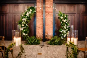Elegant Round Gold Wedding Ceremony Arch with Palm Frond, Monstera Leaf, White Hydrangeas and Roses | Indoor Ceremony Pillar Candles Aisle Decor Ideas | Downtown Tampa Heights Event Venue Armature Works