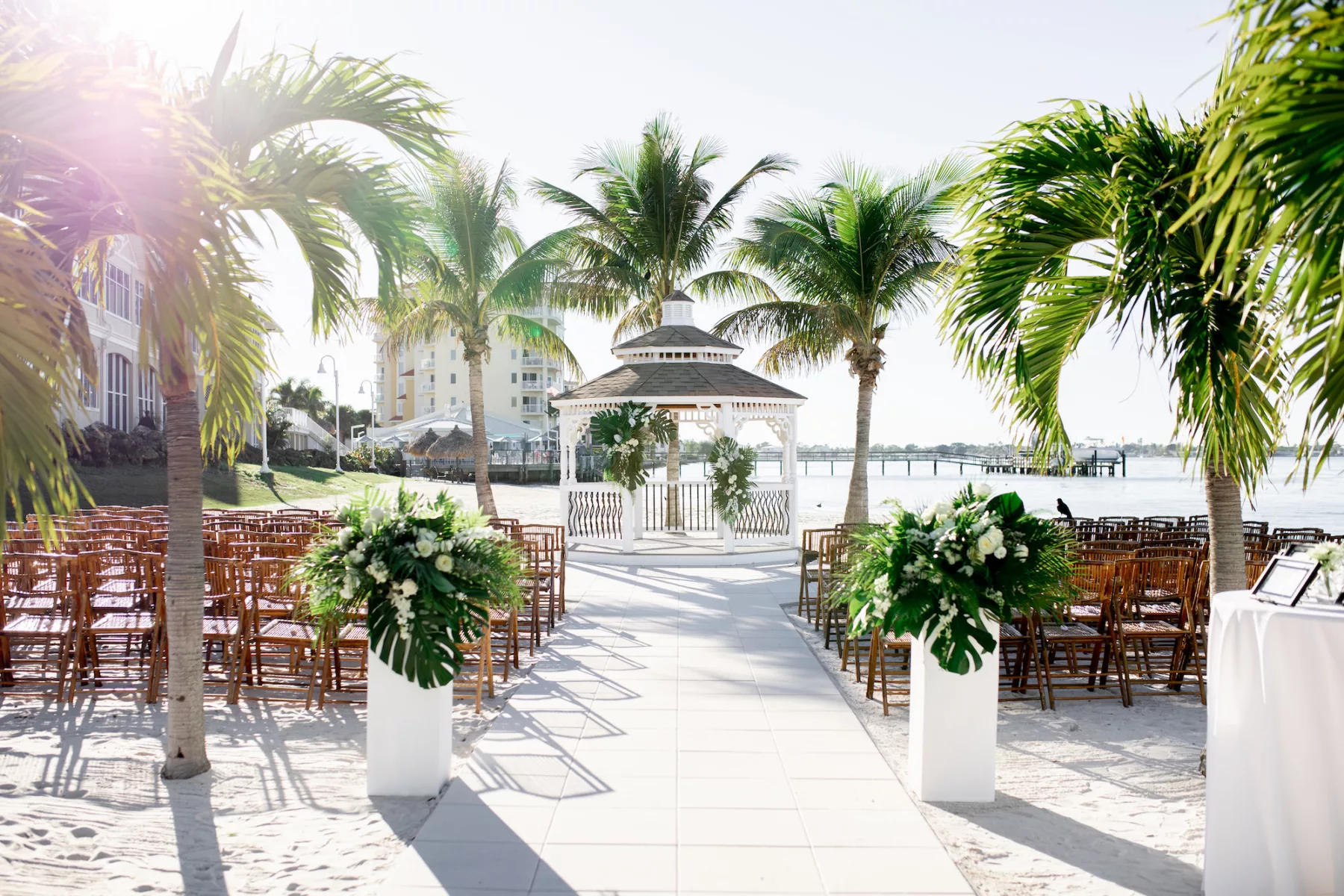 Tropical Private Beach Winter Wedding Ceremony with Gazebo | Bamboo Chairs | Modern White Square Pillars with Monstera, Palm Leaf, and White Roses Aisle Decor | St Pete Event Venue Isla Del Sol Yacht and Country Club