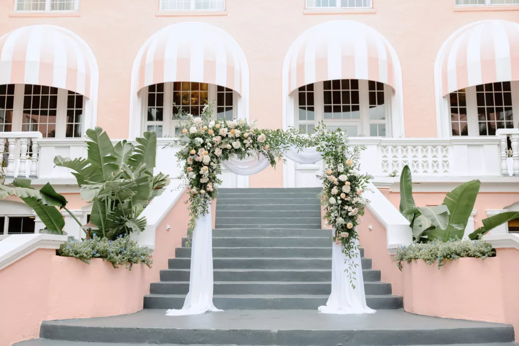 Elegant Outdoor Courtyard Wedding Ceremony Arch with White Drapery, White Roses, Anemone, and Greenery Floral Arrangements | St Pete Event Venue The Don Cesar