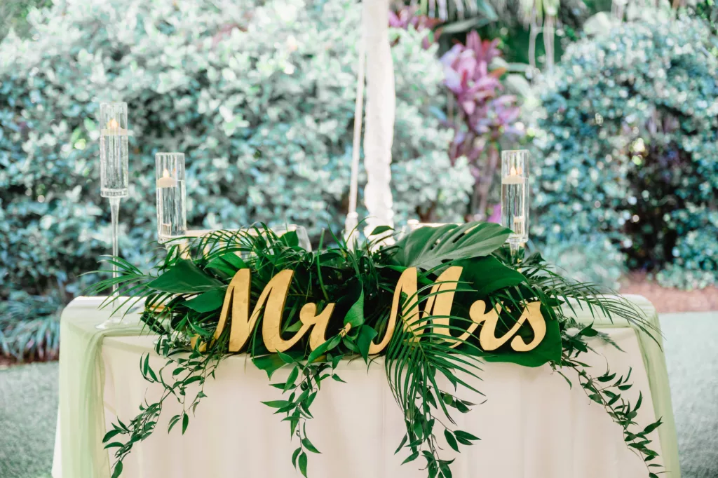 White and Gold Wedding Reception Sweetheart Table Decor Inspiration | Floating Candles, Tropical Greenery Tabletop Arrangement with Palm Fronds and Ferns Ideas | Mr. And Mrs. Sign Inspiration