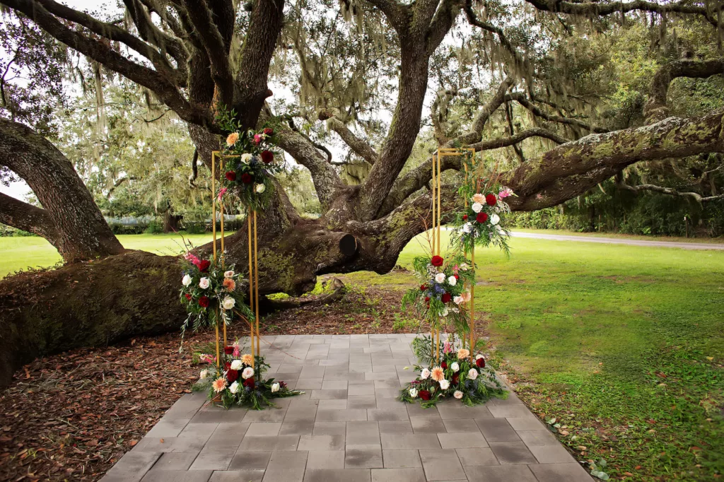 Gold Wedding Ceremony Arch with Red Roses, Blue Thistle, Pink Roses, Peach Chrysanthemums, White Bacopa, and Greenery Fall Decor Ideas | Tampa Bay Florist Save The Date Florida | Event Venue Legacy Lane Weddings