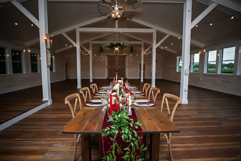 Burgundy Fall Legacy Barn Wedding Reception Inspiration | Rustic Wooden Feasting Table | Red and White Taper Candles, Greenery Garland, and Velvet Table Runner Centerpiece Decor Ideas | Tampa Bay Event Venue Legacy Lane Weddings | Brooksville Florist Save The Date Florida