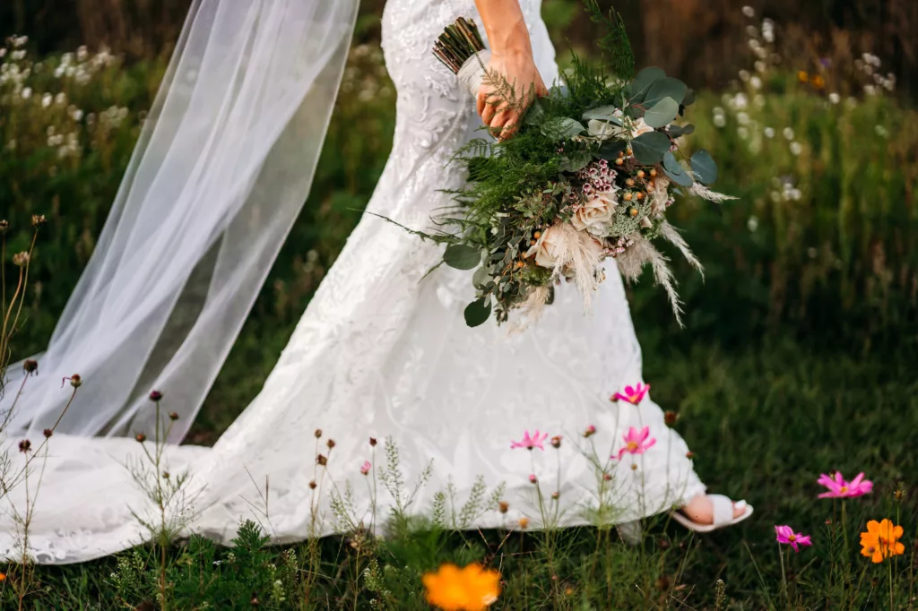 Bride Walking Through Wildflowers | Spring Boho Wedding Bouquet Ideas with Blush Pink Roses, Alyssum, Pampas Grass, and Greenery