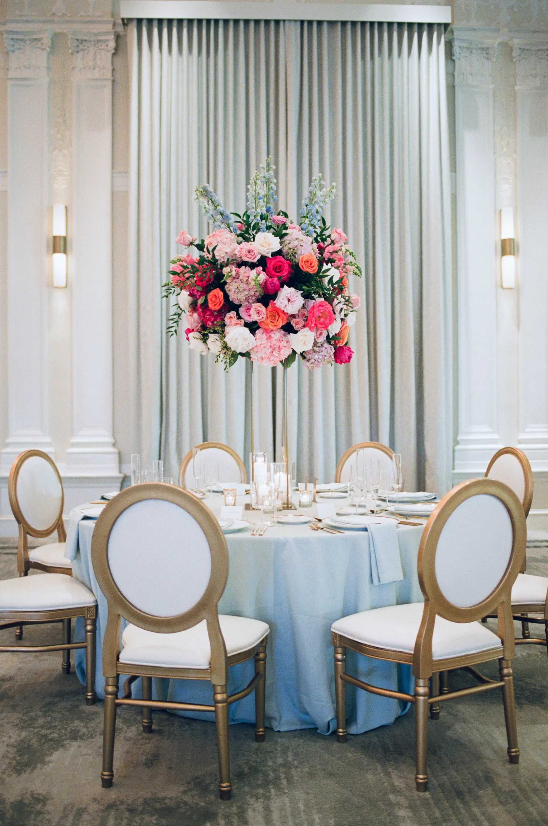 Luxurious Pink and Blue Wedding Reception Tablescape Ideas | Tall Flower Stand with Pink Anemones and Hydrangeas, Orange Garden Roses, Blue Stock Flowers | Gold and White Chairs | Tampa Bay Florist Bruce Wayne Florals | Kate Ryan Event Rentals